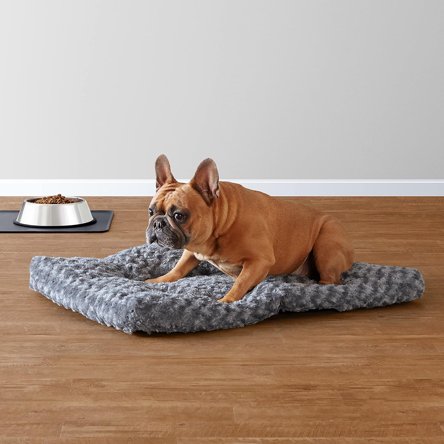 Dog lying on a gray pet bed with a bowl of food nearby on a wooden floor.